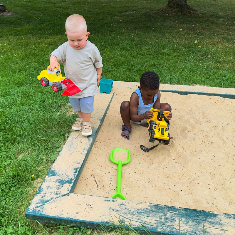 Two children playing with toys in a sandbox outdoors.