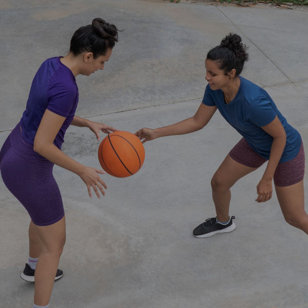 Two women playing with a basketball on a concrete surface