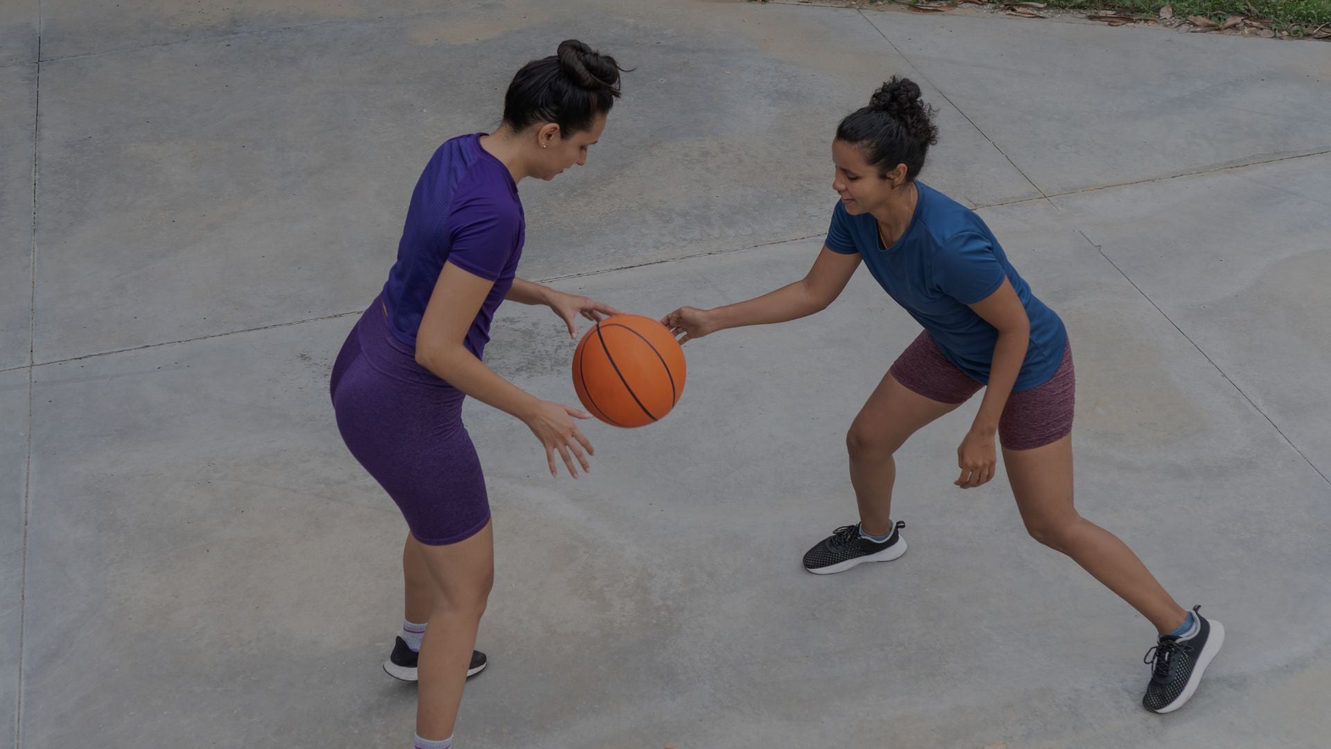 Two women playing basketball on a concrete court